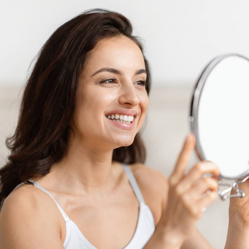 woman looking in mirror at Doctor-led skin health consultation in Colchester